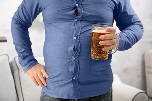 Zoom sur un gros ventre avec une bière à la main illustrant les facteurs de risque du cancer de la prostate